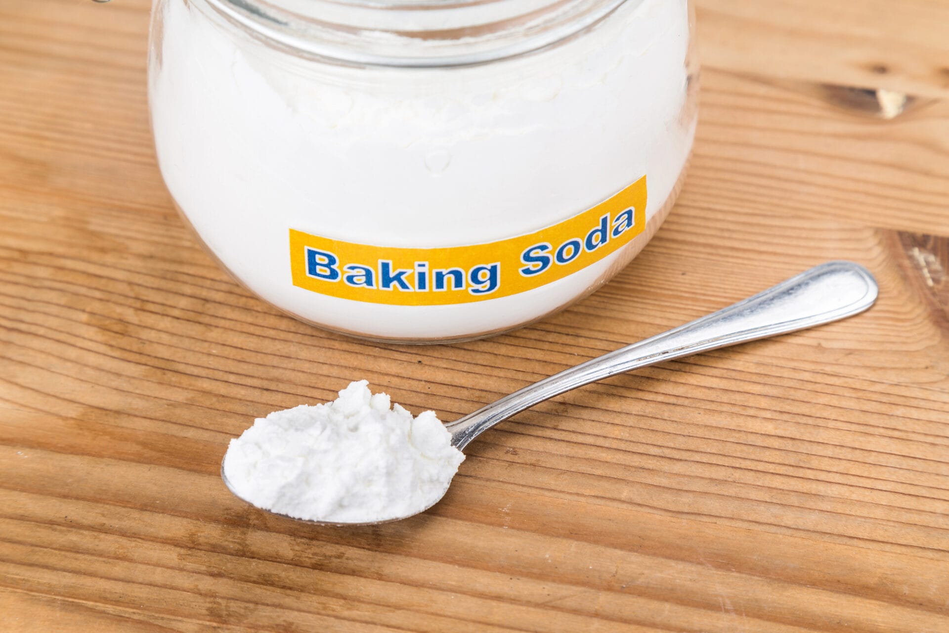 A jar labeled "Baking Soda" sits on a wooden surface, hinting at its versatile uses, such as freshening up clean pillows with a simple sprinkle of the white powder beside it.