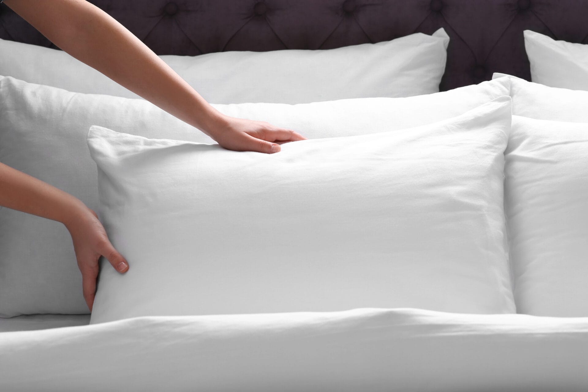 Hands carefully adjusting a white sleeping pillow on a neatly made bed with crisp white linens, highlighting the perfect harmony of comfort and elegance.